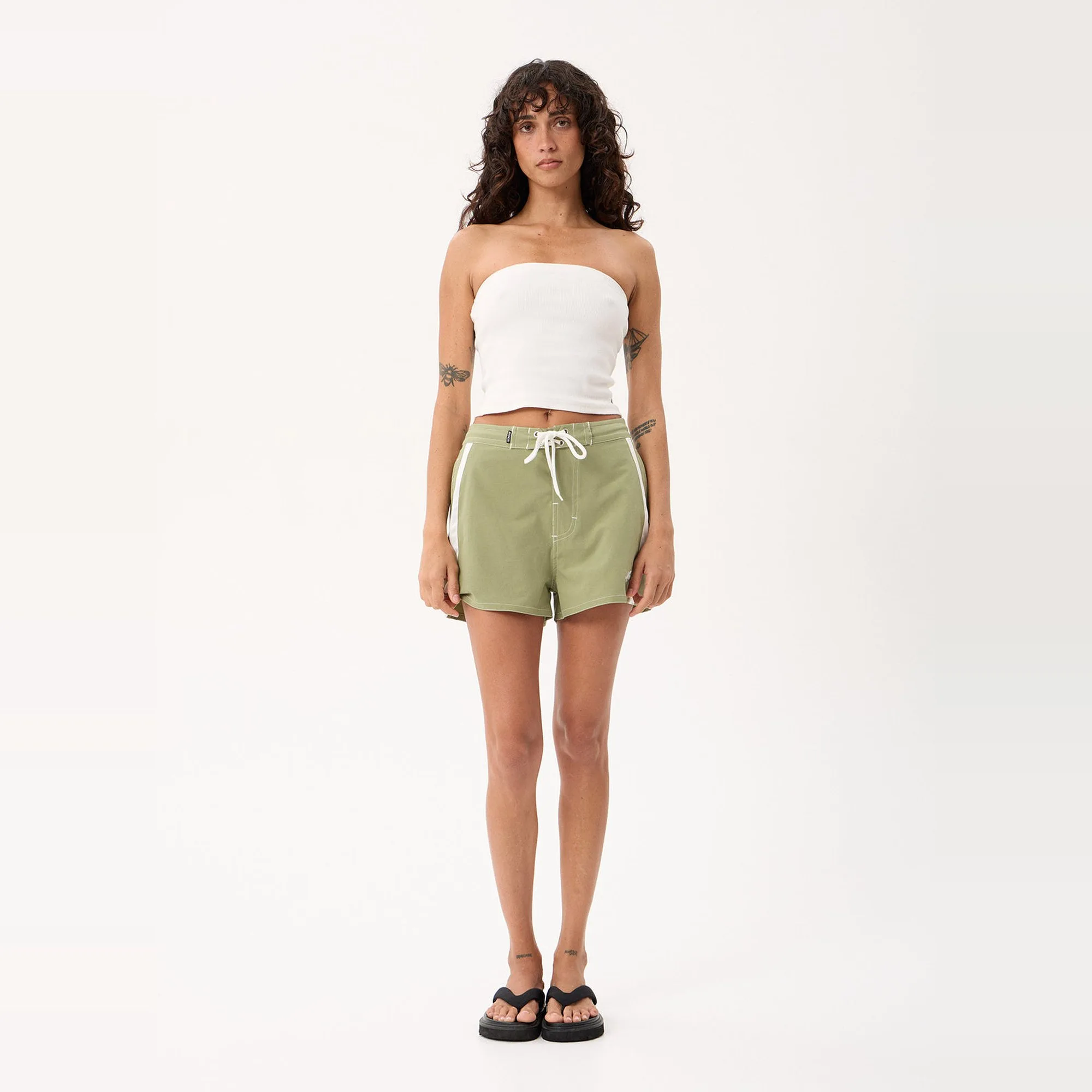 Model wearing the Afends Ellia Boardshorts in Sage with a white tank, full-length front view