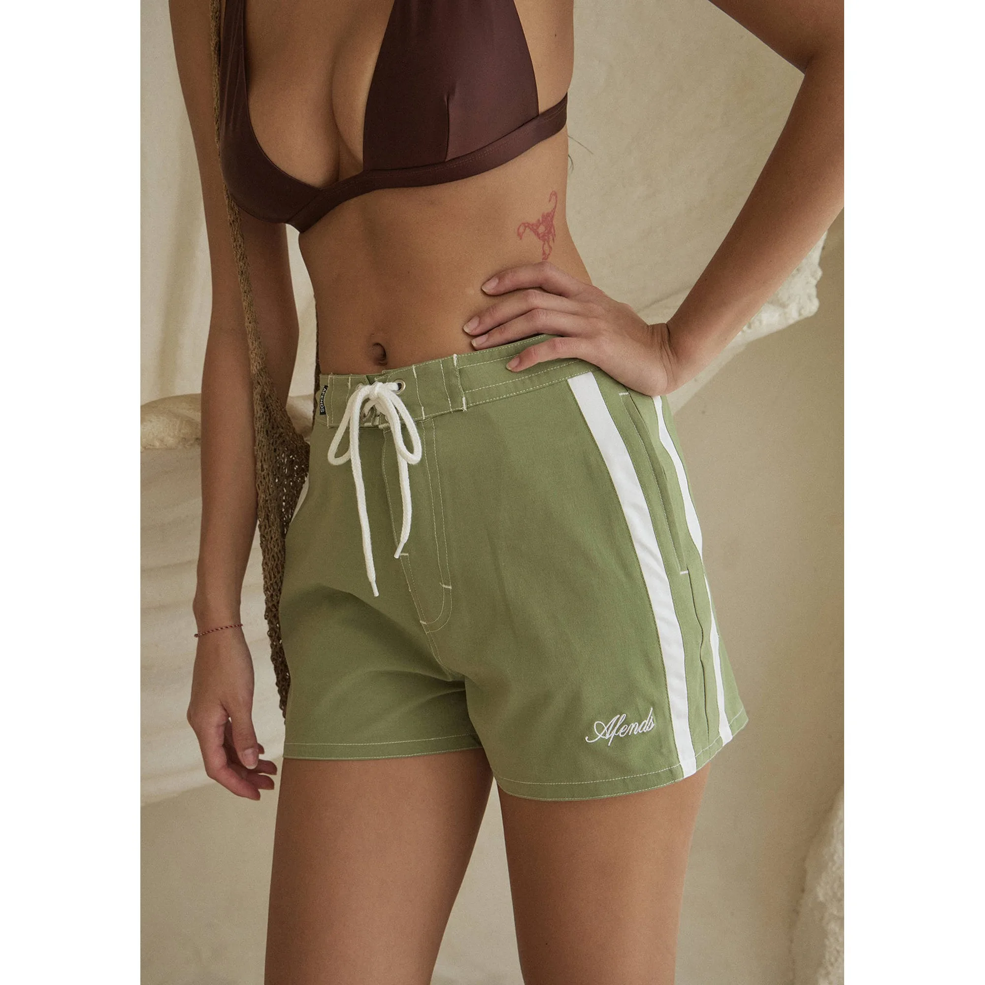 Close-up of the Afends Ellia Boardshorts in Sage with a brown bikini top, showing the flat drawcord and Afends script embroidery