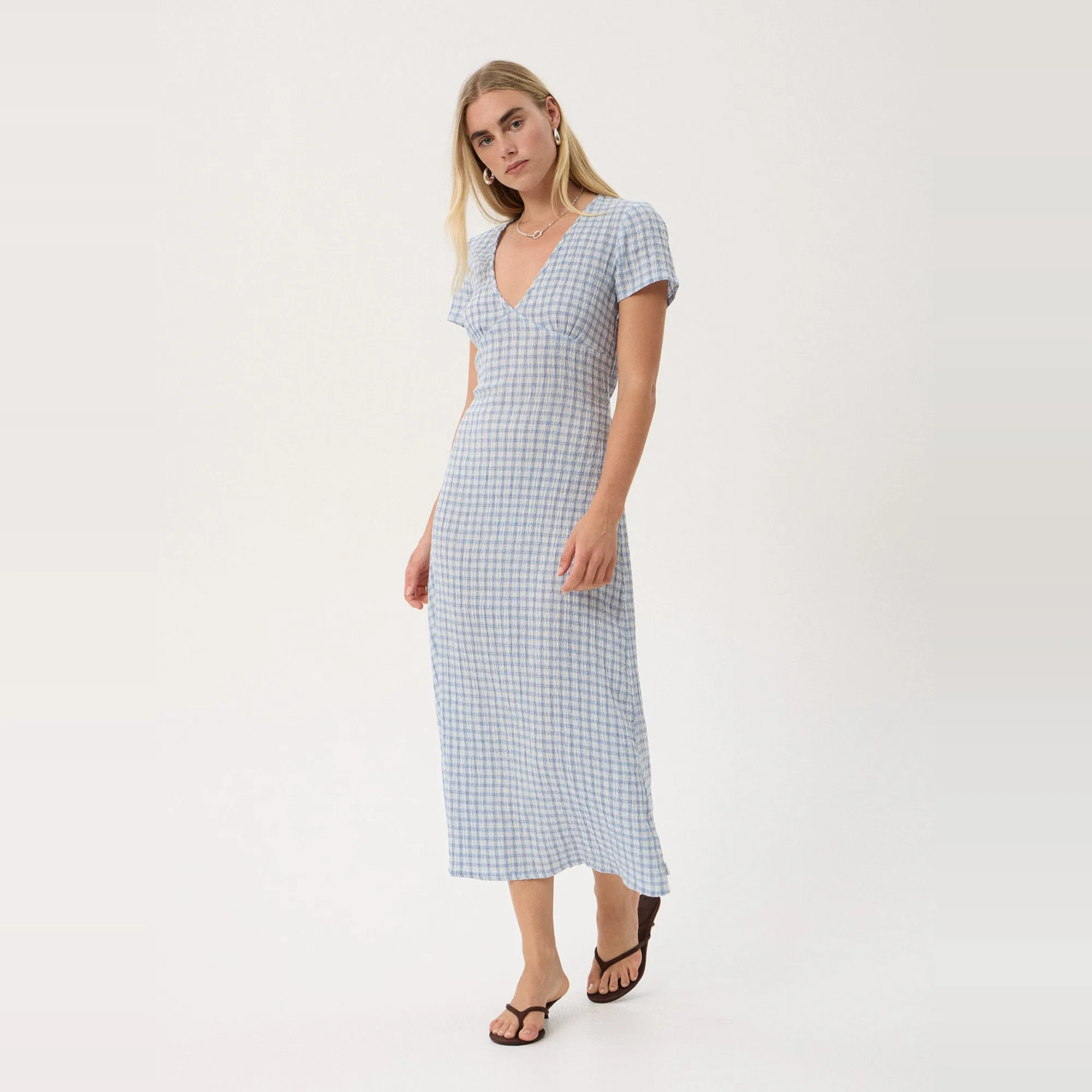 Model in the Afends Maeve Seersucker Maxi Dress in Powder Blue Check, three-quarter view showing the deep V-neck and short sleeves